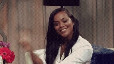 A Woman Is Smiling While Sitting On A Couch Next To A Lamp . GIF