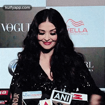 A Woman Is Smiling While Standing In Front Of A Microphone . GIF