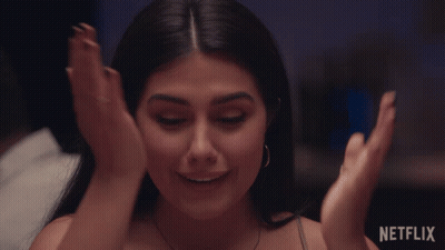 A Woman Is Smiling With Her Hands On Her Face In Front Of A Netflix Sign GIF