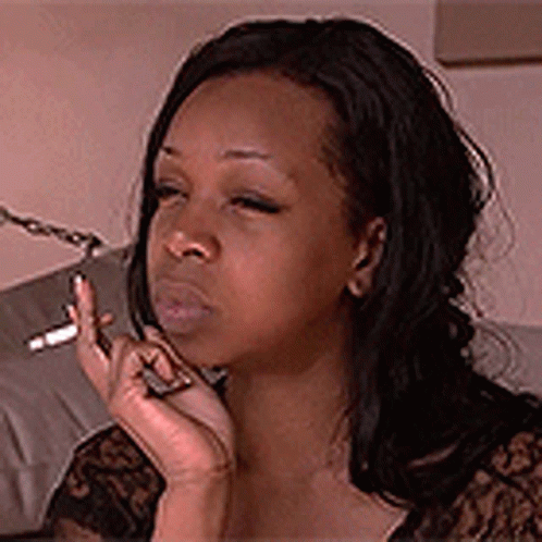 A Woman Is Smoking A Cigarette And Looking At The Camera . GIF