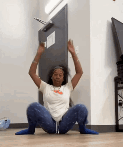 A Woman Is Squatting On The Floor In Front Of A Door With Her Hands In The Air . GIF