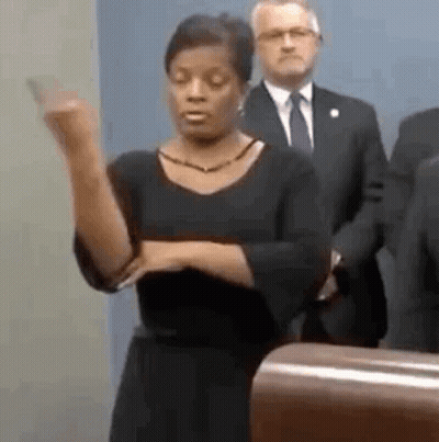A Woman Is Standing At A Podium Giving A Speech While A Man In A Suit Stands Behind Her . GIF