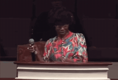 A Woman Is Standing At A Podium Holding A Microphone . GIF