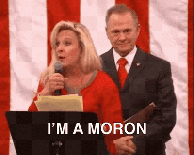 A Woman Is Standing At A Podium Holding A Microphone And A Man Is Behind Her . GIF