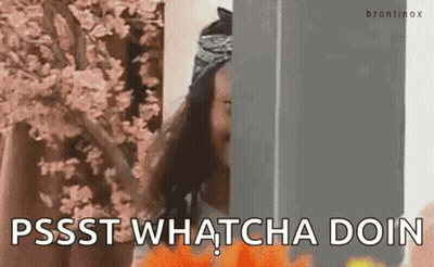 A Woman Is Standing Behind A Wall With Flowers In The Background And Says `` Pssst Whatcha Doin '' . GIF