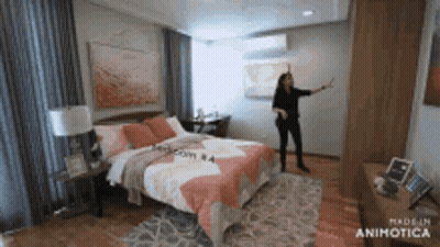 A Woman Is Standing In A Bedroom With A Large Bed . GIF