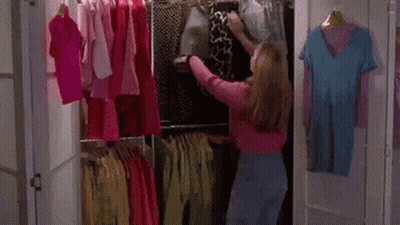 A Woman Is Standing In A Closet Filled With Clothes And Picking A Shirt . GIF