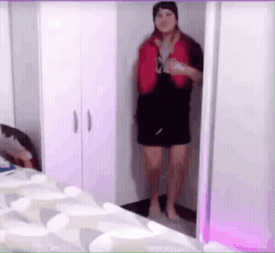 A Woman Is Standing In A Closet Wearing A Red Vest And Black Shorts . GIF
