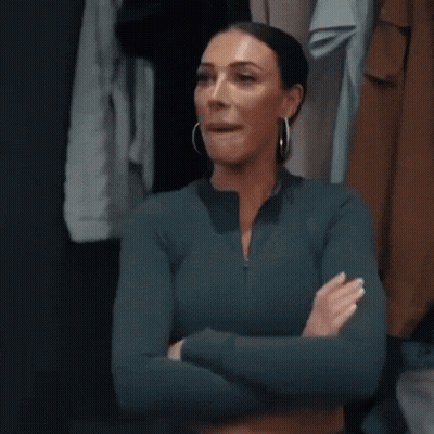 A Woman Is Standing In A Closet With Her Arms Crossed And Looking At The Camera . GIF