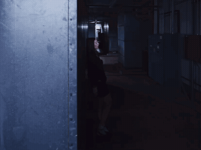 A Woman Is Standing In A Dark Hallway With A Light On GIF