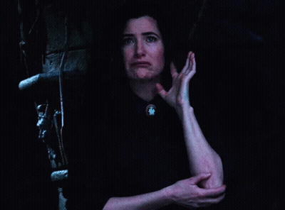 A Woman Is Standing In A Dark Room Holding Her Elbow . GIF