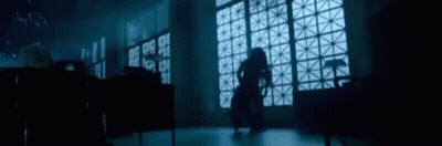 A Woman Is Standing In A Dark Room In Front Of A Large Window . GIF