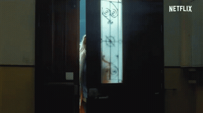 A Woman Is Standing In A Dark Room Looking Out Of A Doorway . GIF