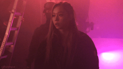 A Woman Is Standing In A Dark Room With Purple Lights And The Words Gifsaespa On The Bottom GIF