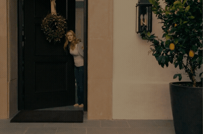 A Woman Is Standing In A Doorway With A Wreath Hanging From It GIF