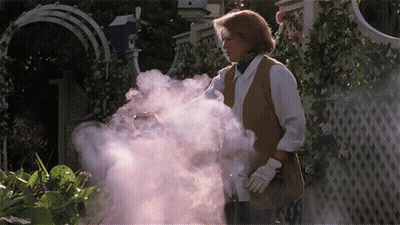 A Woman Is Standing In A Garden With Smoke Coming Out Of Her Hand GIF