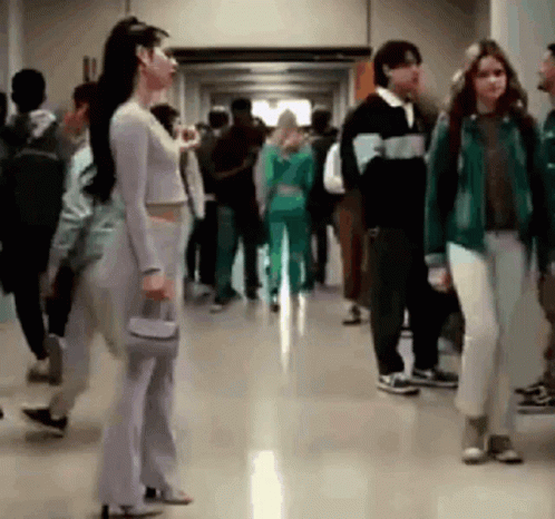 A Woman Is Standing In A Hallway Surrounded By Other People . GIF