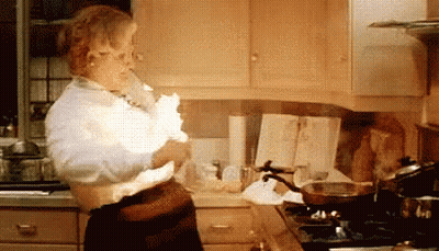 A Woman Is Standing In A Kitchen Holding A Piece Of Paper That Is Exploding . GIF