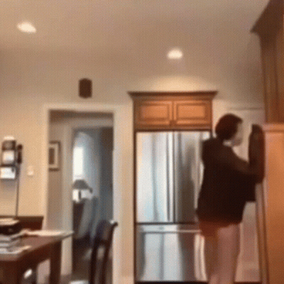 A Woman Is Standing In A Kitchen Next To A Refrigerator . GIF