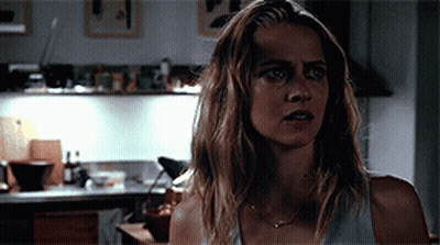 A Woman Is Standing In A Kitchen Wearing A White Tank Top GIF