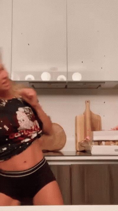 A Woman Is Standing In A Kitchen Wearing Shorts And A Shirt . GIF