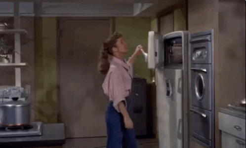 A Woman Is Standing In A Kitchen With Her Back To The Camera . GIF