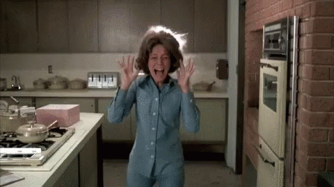 A Woman Is Standing In A Kitchen With Her Mouth Open And Her Hair Flying In The Air . GIF