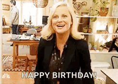A Woman Is Standing In A Living Room And Smiling While Saying `` Happy Birthday ! '' GIF