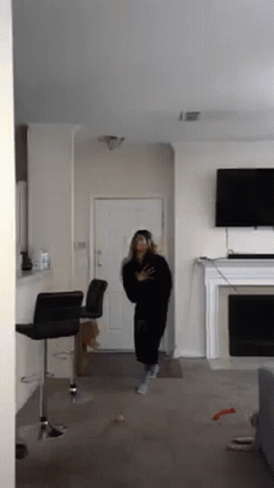 A Woman Is Standing In A Living Room In Front Of A Fireplace And Television . GIF