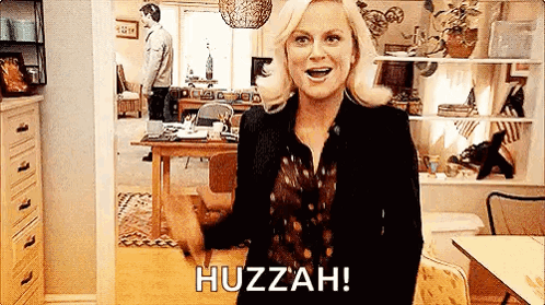 A Woman Is Standing In A Living Room With Her Hands In The Air And A Man Standing In The Background . GIF