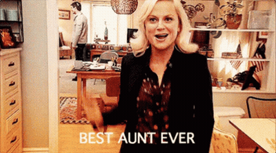 A Woman Is Standing In A Living Room With The Words `` Best Aunt Ever '' On Her Shirt . GIF
