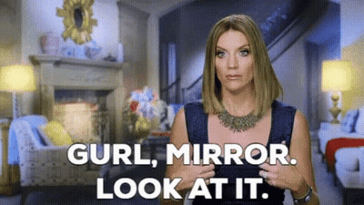 A Woman Is Standing In A Living Room With The Words " Curl Mirror Look At It " GIF
