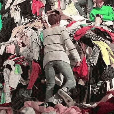 A Woman Is Standing In A Pile Of Clothing GIF