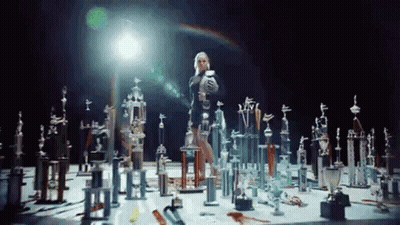 A Woman Is Standing In A Room Filled With Trophies And Awards . GIF