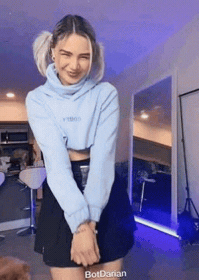 A Woman Is Standing In A Room Wearing A Blue Sweater And A Black Skirt . GIF