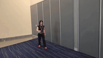 A Woman Is Standing In A Room With A Blue Carpet And A Gray Wall GIF