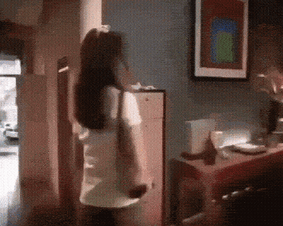 A Woman Is Standing In A Room With A Picture On The Wall Above Her GIF