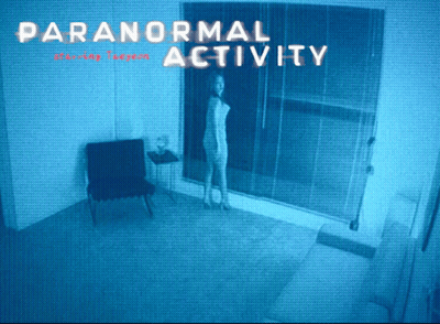 A Woman Is Standing In A Room With The Words Paranormal Activity GIF