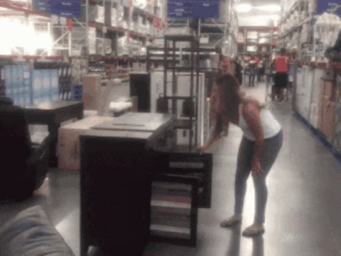 A Woman Is Standing In A Store Looking At A Cabinet GIF
