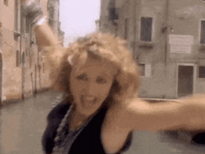 A Woman Is Standing In A Street With Her Arms Outstretched And A Building In The Background . GIF