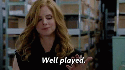 A Woman Is Standing In A Warehouse And Saying `` Well Played '' With Her Hand . GIF