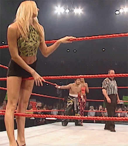 A Woman Is Standing In A Wrestling Ring With A Referee Watching GIF