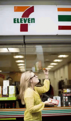 A Woman Is Standing In Front Of A 7 Eleven GIF