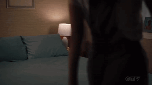 A Woman Is Standing In Front Of A Bed In A Bedroom With A Lamp . GIF
