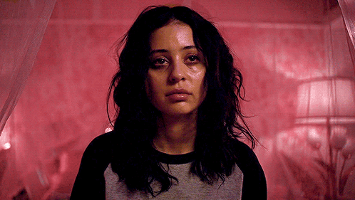 A Woman Is Standing In Front Of A Bed With A Red Curtain . GIF