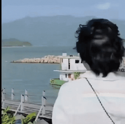 A Woman Is Standing In Front Of A Body Of Water . GIF