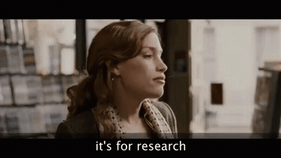 A Woman Is Standing In Front Of A Bookshelf In A Bookstore And Talking About Research . GIF