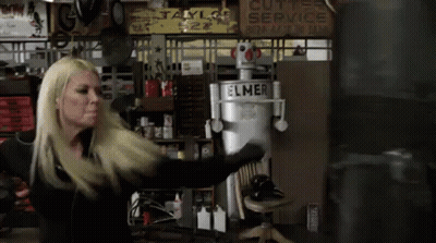 A Woman Is Standing In Front Of A Boxing Bag In A Garage . GIF