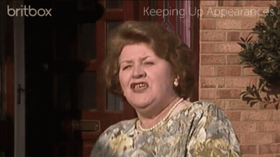 A Woman Is Standing In Front Of A Brick Wall With The Words Britbox Keeping Up Appearances Behind Her GIF