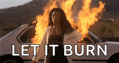 A Woman Is Standing In Front Of A Car On Fire . GIF